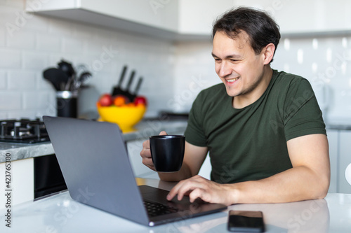Handsome man sitting at desk working from home on laptop in the kitchen