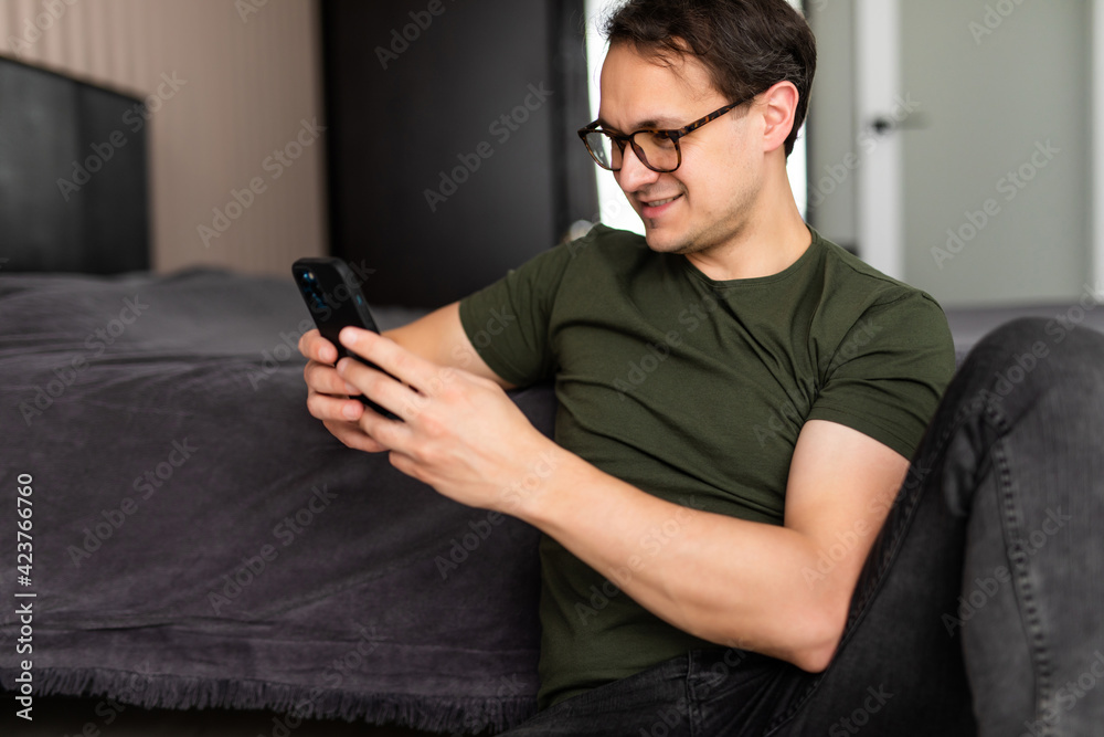 Obraz premium Happy young relaxed man at home using phone sitting on the floor in bedroom