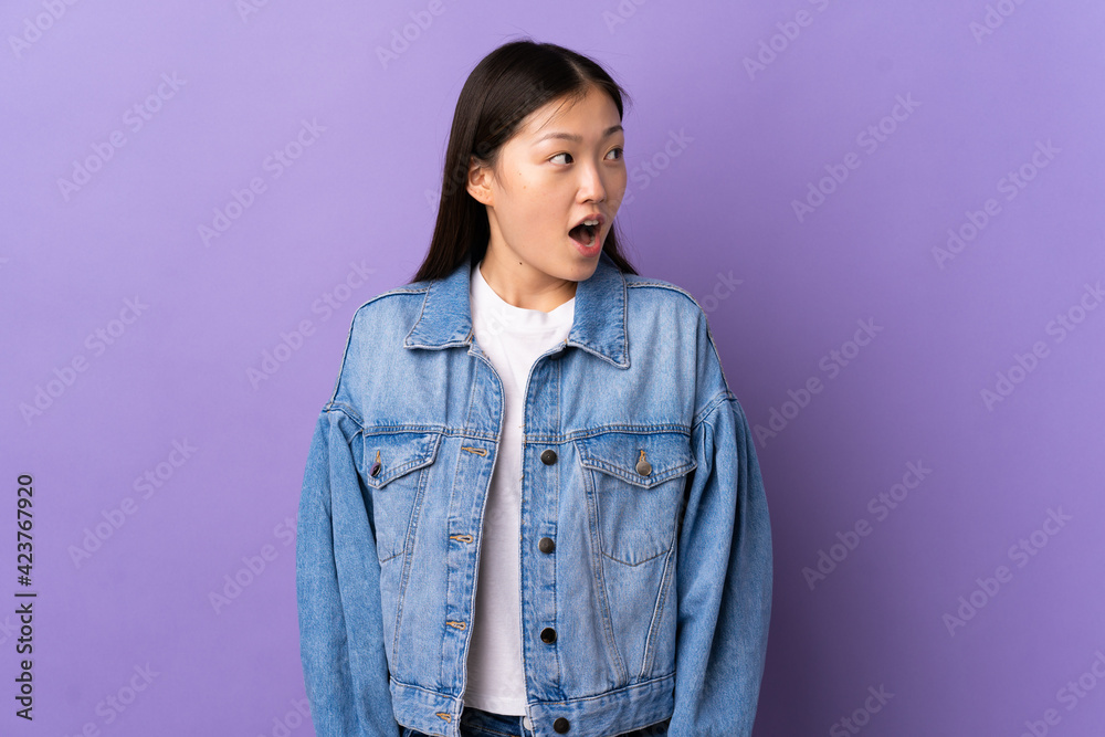 Young Chinese girl over isolated purple background doing surprise gesture while looking to the side Young Chinese girl over isolated purple background doing surprise gesture while looking to the side