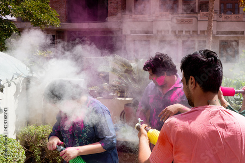people, men women throwing colorful dust powder at each other on the indian hindu festival of holi while playing safely during the pandemic