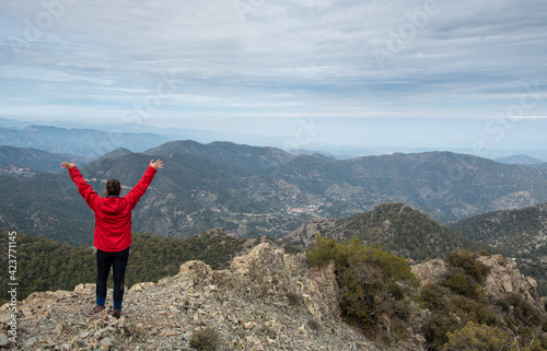 Tourist woman with raised arms standing on rocky top against a cloudy sky enjoying mountain range panorama. © Michalis Palis