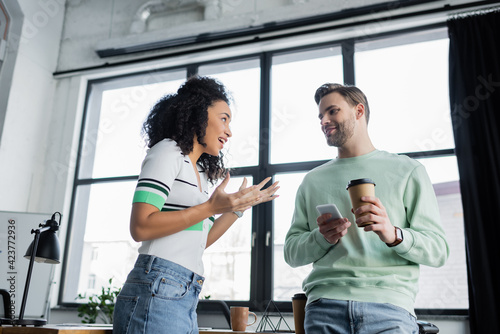 excited african american businesswoman gesturing while talking to smiling colleague