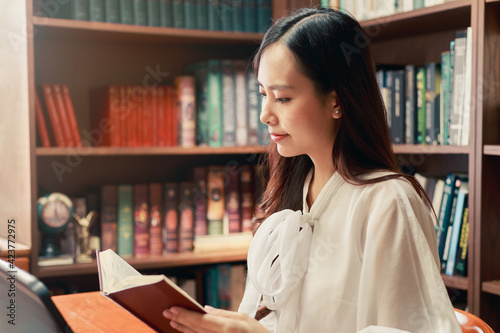 Happy Asian young knowledgable business woman reading the book in library with various book with books on the bookshelf background photo