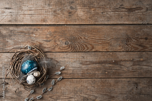 nest with Easter eggs, feathers and pussy willow twigs on a wooden background. space for text