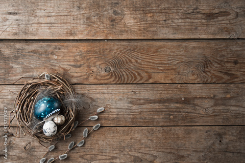 nest with Easter eggs, feathers and pussy willow twigs on a wooden background. space for text photo