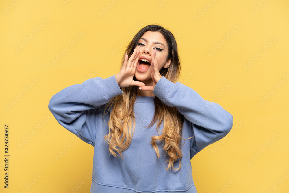Young Russian girl isolated on yellow background shouting and announcing something Young Russian girl isolated on yellow background shouting and announcing something