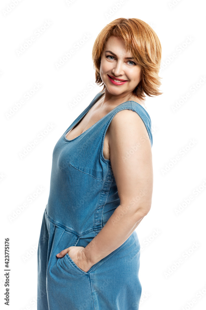 Beautiful smiling middle aged woman with red hair in denim overalls. Self-care and health. Isolated on white background. Vertical. Beautiful smiling middle aged woman with red hair in denim overalls. Self-care and health. Isolated on white background. Vertical.