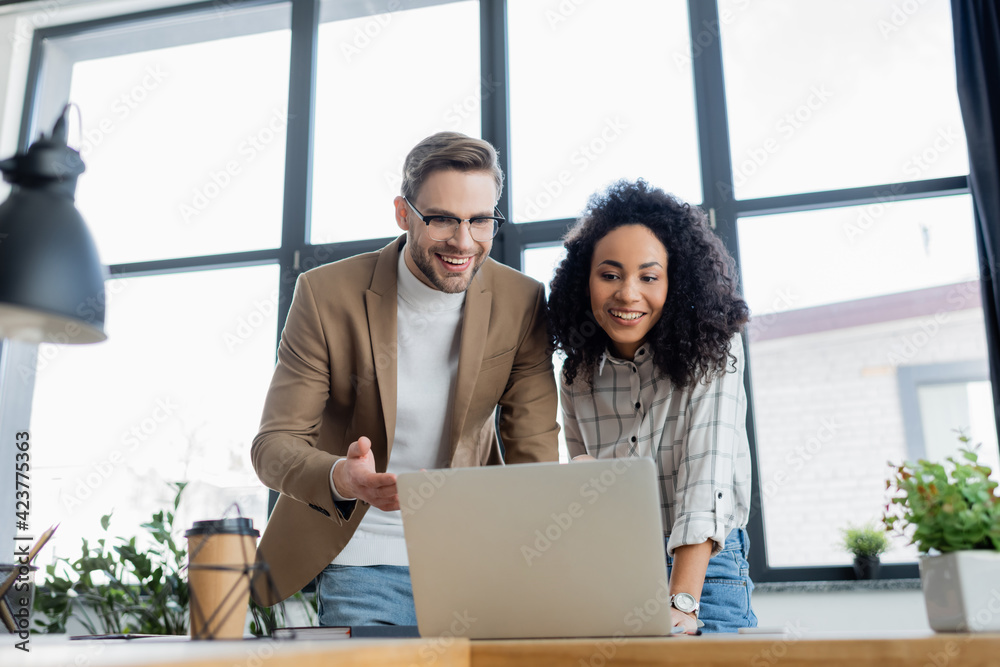 Multiethnic business people using laptop near plant and coffee to go on blurred foreground Multiethnic business people using laptop near plant and coffee to go on blurred foreground
