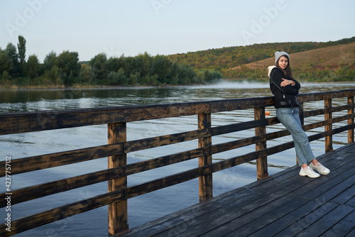 Young woman in casual warm outfit posing near lake