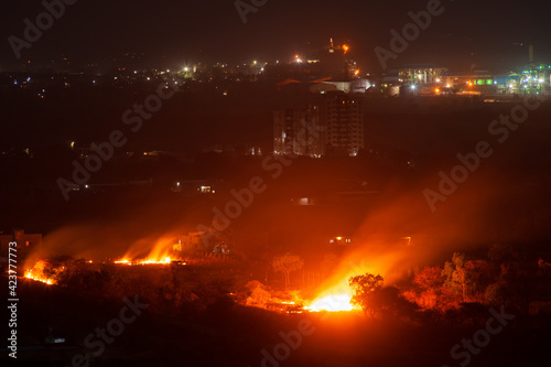 Stubble burn fire in the farm field, city at the backdrop. © Pritha_EasyArts