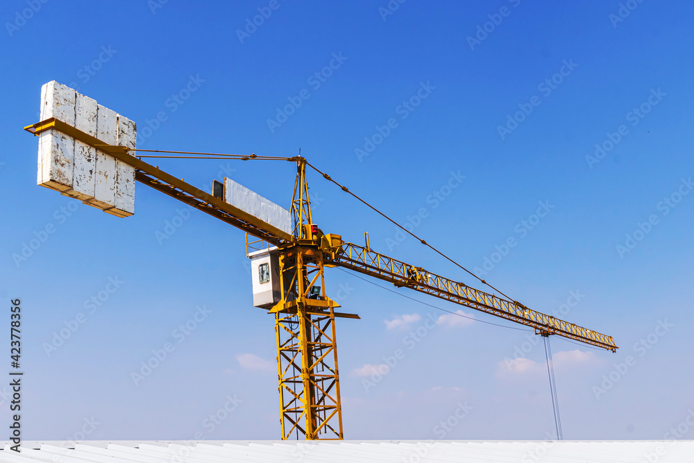 The construction crane with the cloud sky background at the construction site. The Tower Crane against a blue sky. Yellow hoisting crane on blue sky background with clouds, close up.