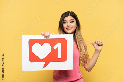 Young Russian girl isolated on yellow background holding a placard with Like icon with proud gesture