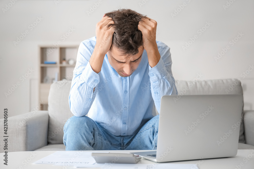 Stressed man with laptop and calculator at home. Bankruptcy concept Stressed man with laptop and calculator at home. Bankruptcy concept