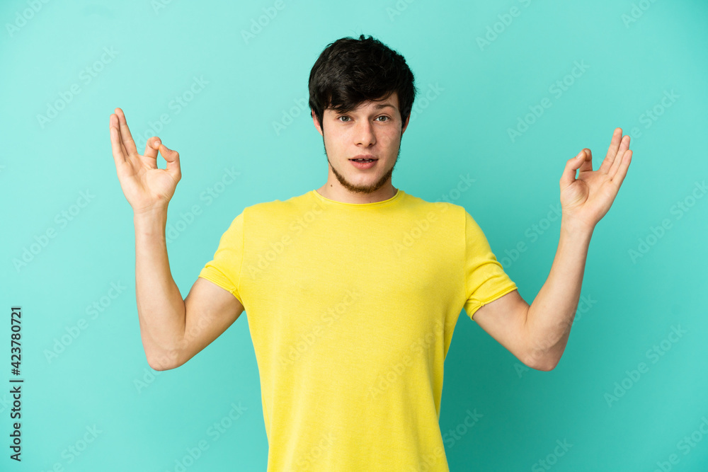 Young Russian man isolated on blue background in zen pose Young Russian man isolated on blue background in zen pose