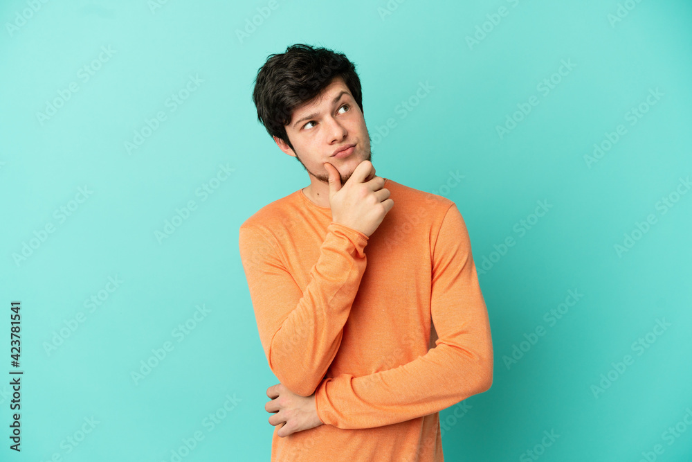 Young Russian man isolated on blue background having doubts