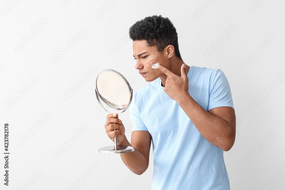 African-American teenage boy applying remedy for acne against light background African-American teenage boy applying remedy for acne against light background