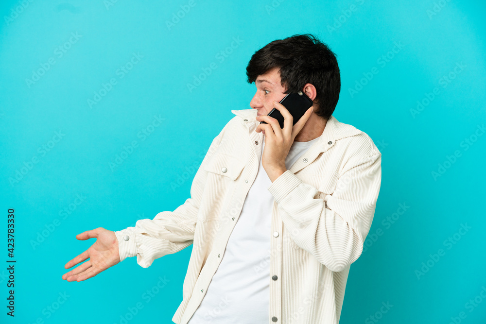 Young Russian man using mobile phone isolated on blue background with surprise expression while looking side Young Russian man using mobile phone isolated on blue background with surprise expression while looking side
