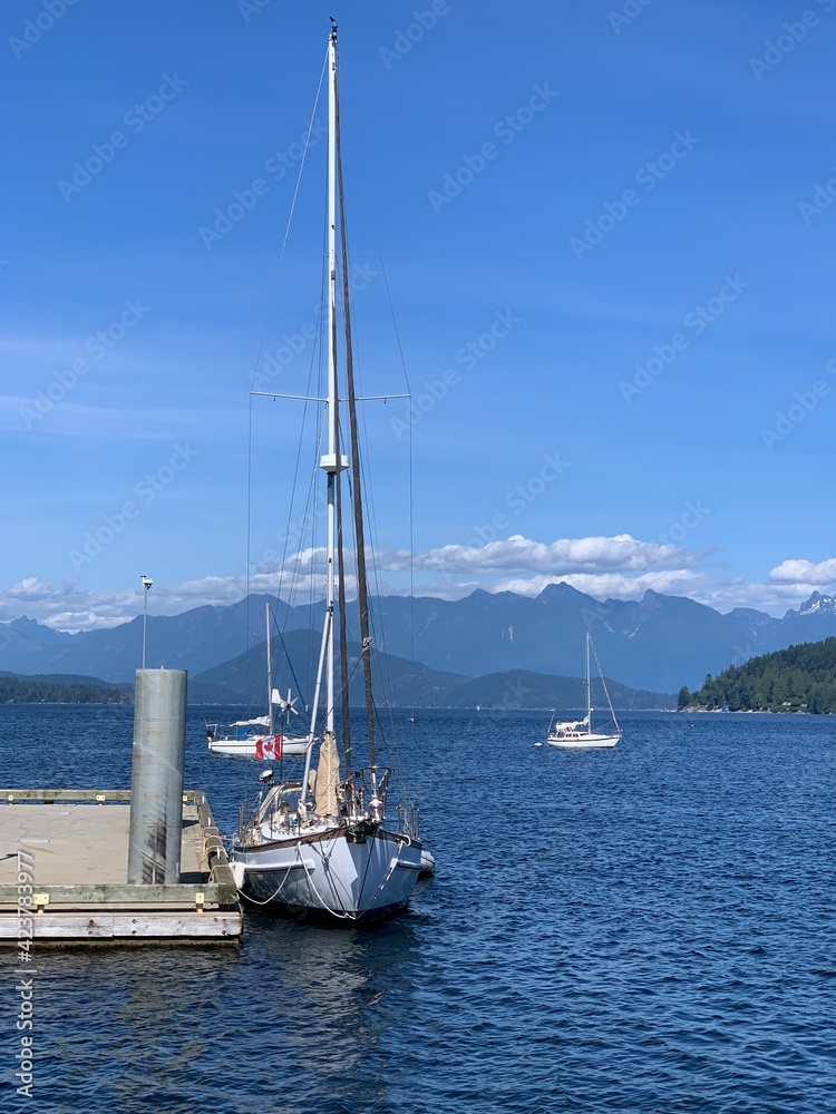 Amazing scene of a sailboat with Canada flag, docking at a marina, the beautiful sea, the distant mountains and islands make this place very special. Amazing scene of a sailboat with Canada flag, docking at a marina, the beautiful sea, the distant mountains and islands make this place very special.