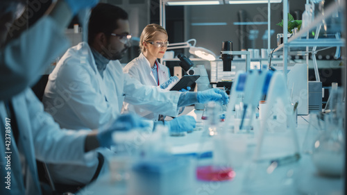 Female Research Scientist Uses Digital Tablet Computer to Enter Experiment Data in a Modern Laboratory. Scientists are Conducting Research with the Help of Technology, Microscope and Micropipettes.