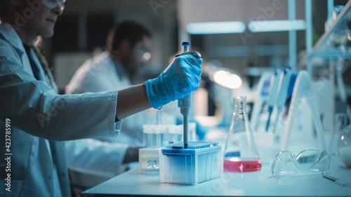 Female Research Scientist Uses Micropipette to Mix Liquids in a Sample Test Tube in a Modern Laboratory. Scientists are Conducting Research with the Help of Technology, Microscope and Tablet Computer.