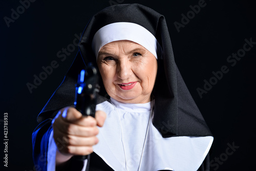 Senior nun with gun on dark...