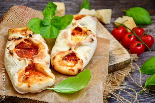 Home made italian mini calzone salami pizza with tomatoes, mozzarella and parmesan cheese and fresh basil 