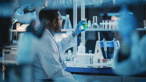 Shot of an Indian Male Working on DNA, Analyzing Green Samples in a Petri Dish. He is Using Microscope and Working in a Modern Applied Science Laboratory.
