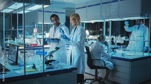 Tableau sur toile Female and Male Medical Research Scientists Have a Conversation While Conducting Experiments in Sample Test Tubes, Writing Analysis Results on a Tablet Computer