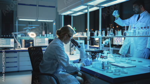 Medical Research Scientist Looks at Biological Samples Under Digital Microscope in Applied Science Laboratory. Beautiful Caucasian Lab Engineer in White Coat Working on Vaccine and Medicine.