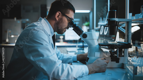 Medical Development Laboratory: Caucasian Female Scientist Looking Under Microscope, Analyzes Petri Dish Sample. Specialists Working on Medicine, Biotechnology Research in Advanced Laboratory