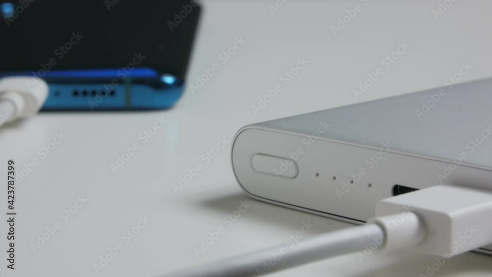 Powerbank external battery charging smartphone lying on the table. The indicator flashes. Powerbank external battery charging smartphone lying on the table. The indicator flashes.