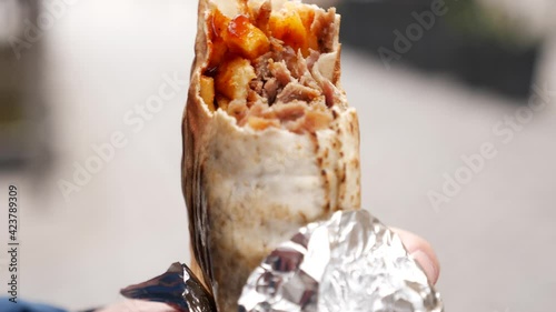 A Man eats Kebab on a Street Food taking with Hands with Meat, Potato and Vegetables