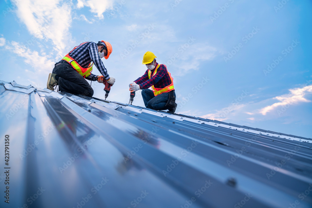 Tow construction worker safety wear using electric drill tools install on new roof metal sheet, Roof construction concept. Tow construction worker safety wear using electric drill tools install on new roof metal sheet, Roof construction concept.