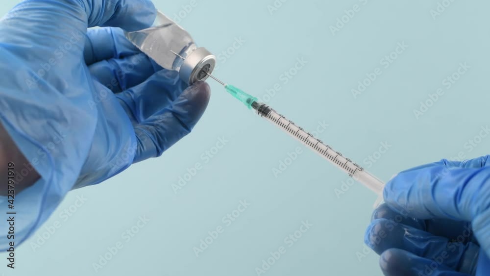 closeup of gloved hands loading vaccine from vial on blue background closeup of gloved hands loading vaccine from vial on blue background