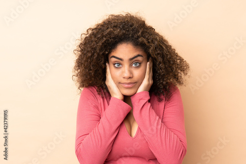 Young African American woman isolated on beige background frustrated and covering ears
