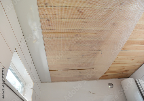 Bathroom renovation: Installing PVC ceiling cladding, plastic ceiling panels over a vapor barrier membrane and planked wood ceiling in a bathroom.