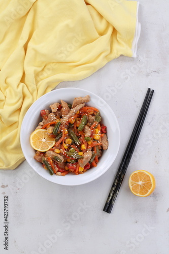 Meat with vegetables and sesame seeds on gray background with yellow cloth