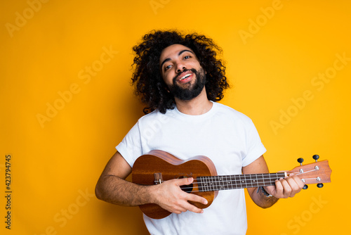 Happy african american man in white t-shirt playing ukulele cheerfully smiling broadly