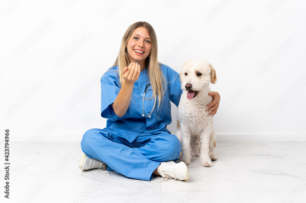 Young veterinarian woman with dog sitting on the floor inviting to come with hand. Happy that you came