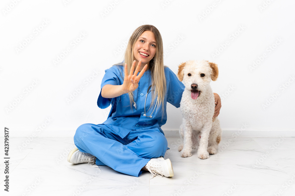 Young veterinarian woman with dog sitting on the floor happy and counting four with fingers