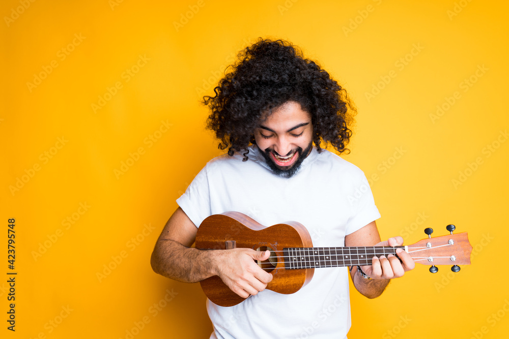Obraz premium A cute young egyptian man with a beard holds a small guitar in his hands and plays it