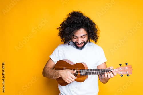 A cute young egyptian man with a beard holds a small guitar in his hands and plays it