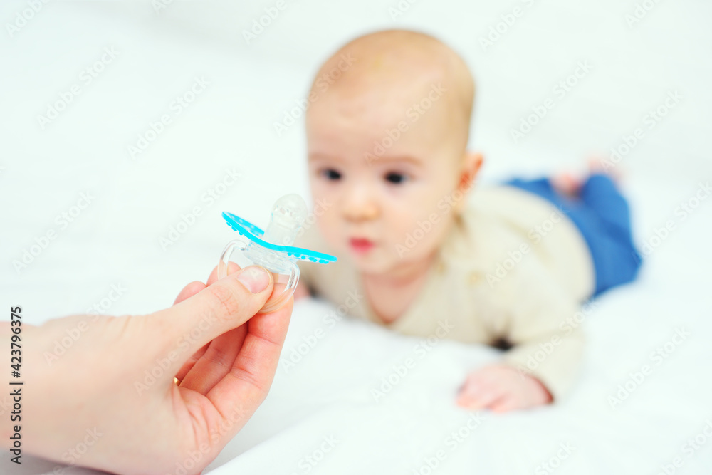 mom's hand gives a pacifier to her baby son on a white background. mom's hand gives a pacifier to her baby son on a white background.