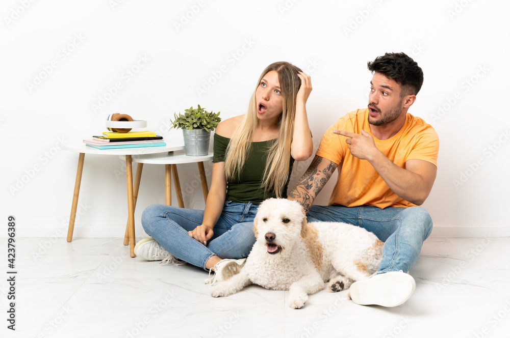 Young caucasian couple with dog staying at home pointing finger to the side with a surprised face Young caucasian couple with dog staying at home pointing finger to the side with a surprised face