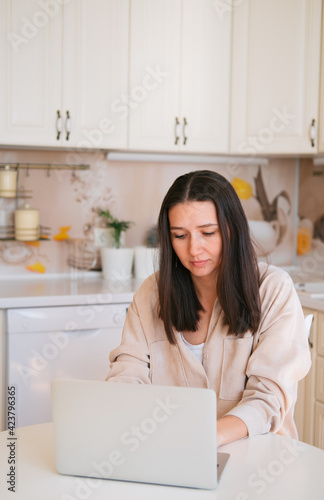 Young beautiful caucasian woman using laptop, sitting in kitchen.