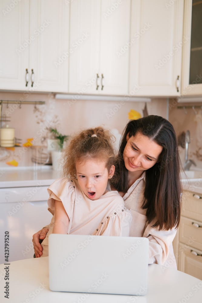 Cute portrait of mother and daughter sitting in a kitchen table and using computer. Cute portrait of mother and daughter sitting in a kitchen table and using computer.
