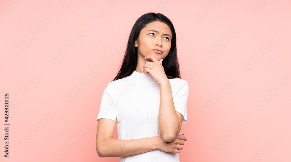 Teenager Chinese woman isolated on pink background having doubts Teenager Chinese woman isolated on pink background having doubts