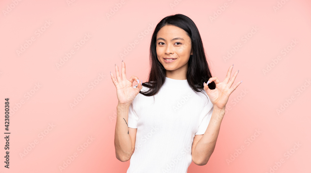 Teenager Chinese woman isolated on pink background showing ok sign with two hands Teenager Chinese woman isolated on pink background showing ok sign with two hands