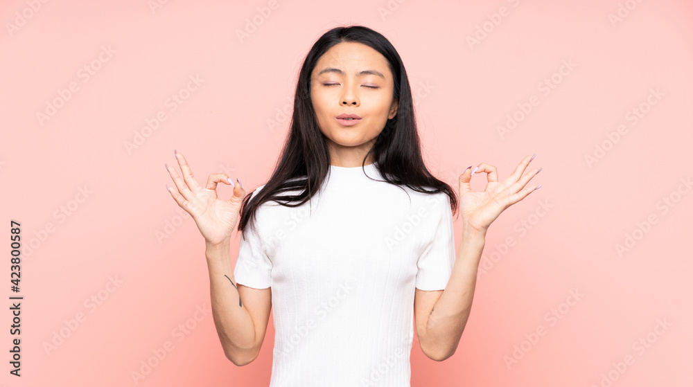 Teenager Chinese woman isolated on pink background in zen pose Teenager Chinese woman isolated on pink background in zen pose