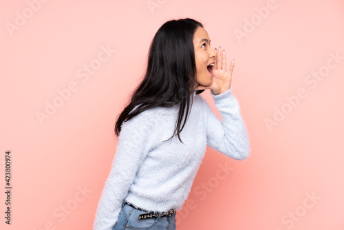 Teenager Chinese woman isolated on pink background shouting with mouth wide open to the side